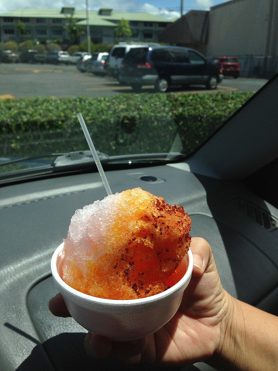 Hawaiian shave ice with colorful syrup flavors in a paper cone.